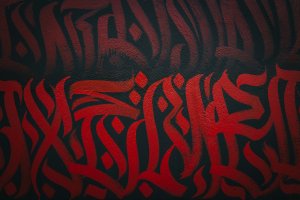 L'artiste REID entrain de peindre LE MUR avec un pinceau utilisant une couleur rouge.