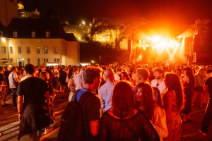 Image de la scène dans l'Abtei Neimënster dans le noir avec des illuminations sur scène et un grand nombre de public devant la scène en train de regarder le concert