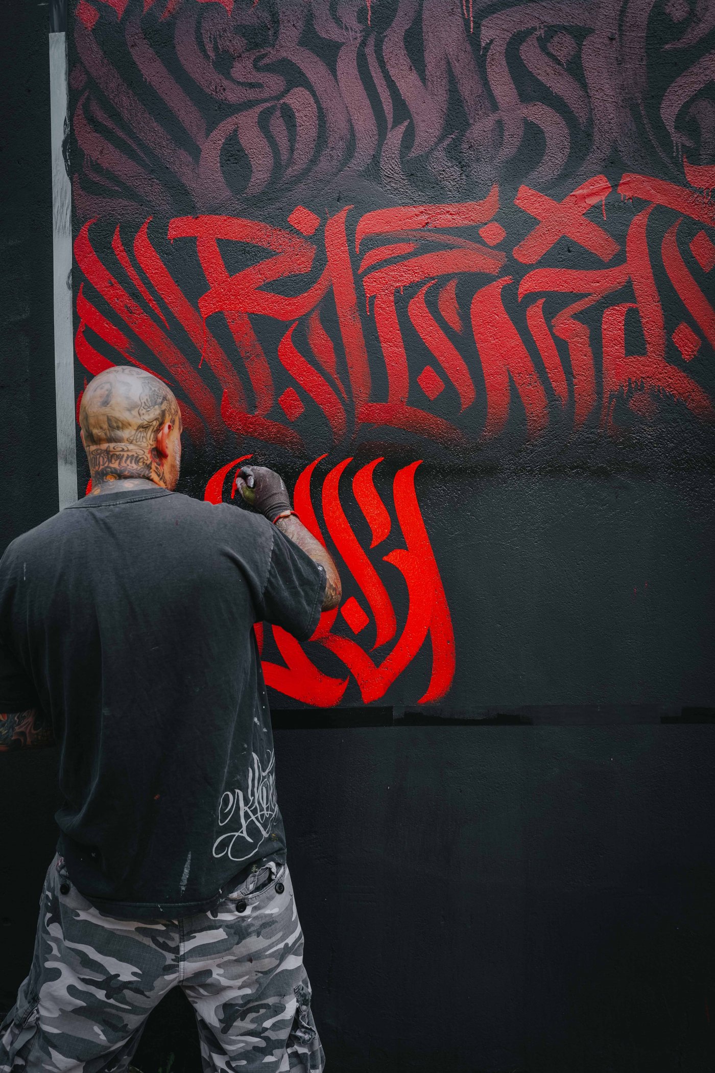L'artiste REID entrain de peindre LE MUR avec un pinceau utilisant une couleur rouge.
