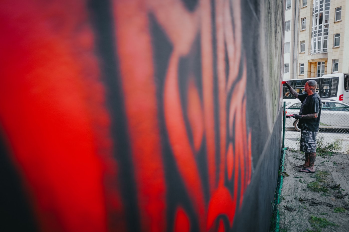 L'artiste REID entrain de peindre LE MUR avec un pinceau utilisant une couleur rouge.