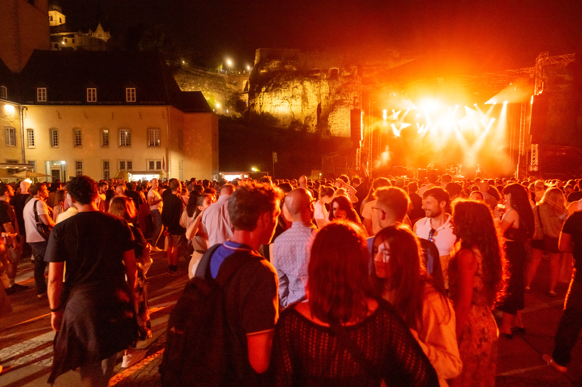 Image de la scène dans l'Abtei Neimënster dans le noir avec des illuminations sur scène et un grand nombre de public devant la scène en train de regarder le concert