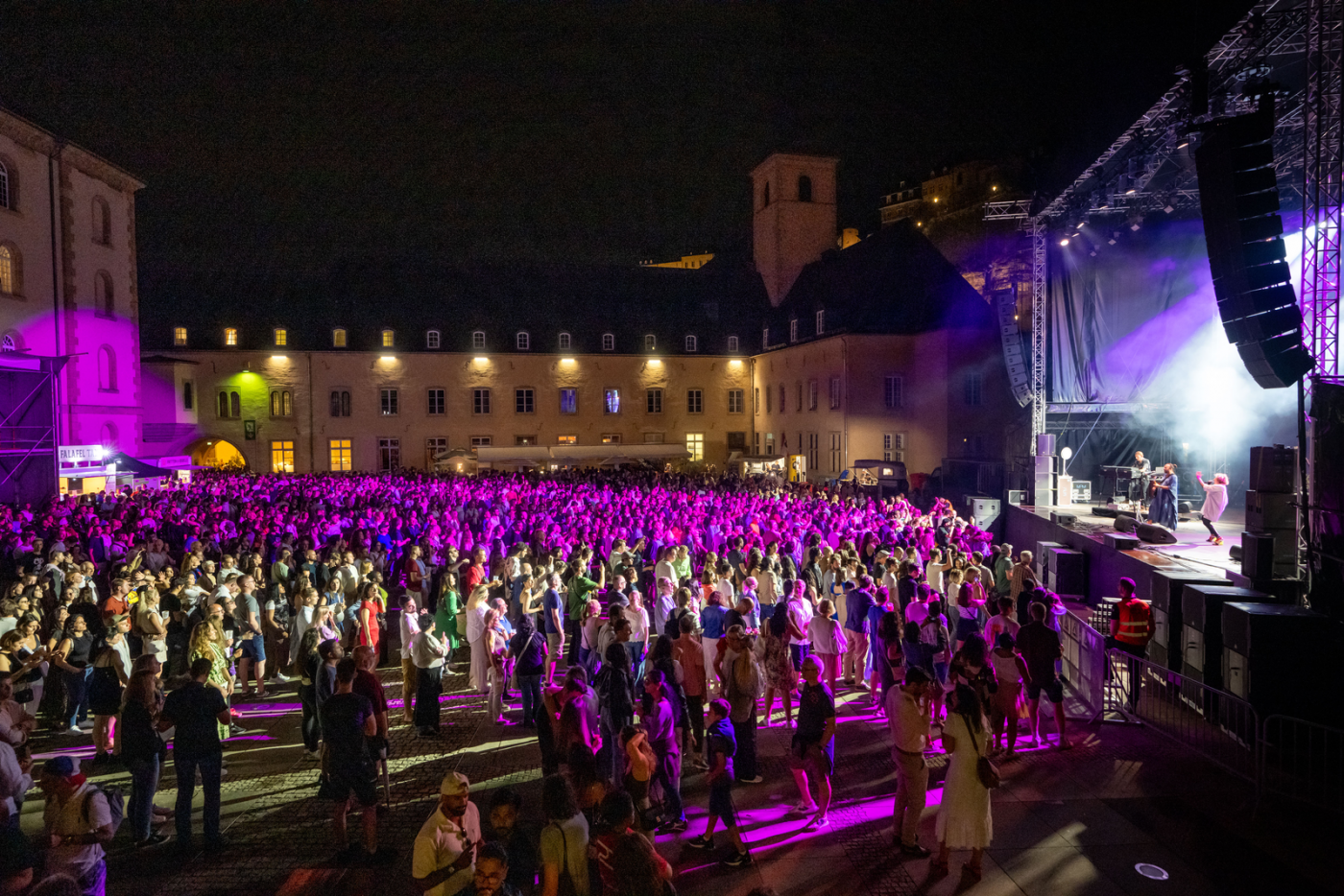 Image de la scène dans l'Abtei Neimënster dans le noir avec des illuminations sur scène et un grand nombre de public devant la scène en train de regarder le concert