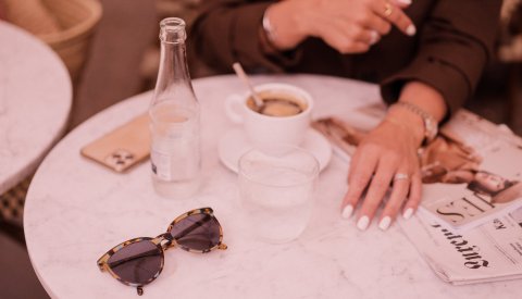 lunettes de soleil, bouteille d'eau, journal et café sur une table d'une terrasse